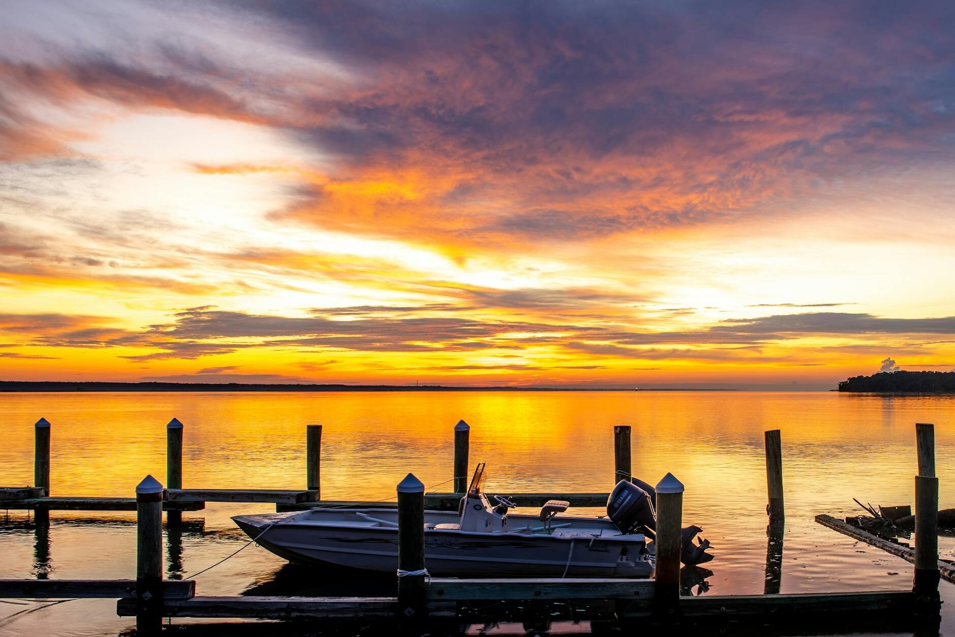 Gulf Coast sunset over calm water — plum clouds, magenta horizon, and gold reflections on the bay.