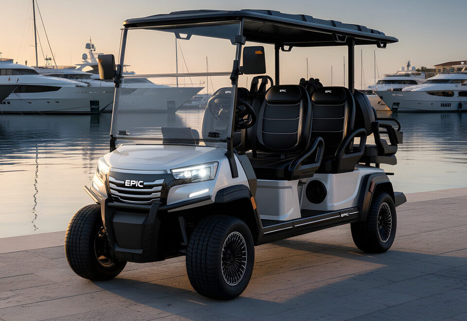 A white EPIC six-passenger golf cart parked on a marina quay at golden hour, yachts and calm Gulf water behind.