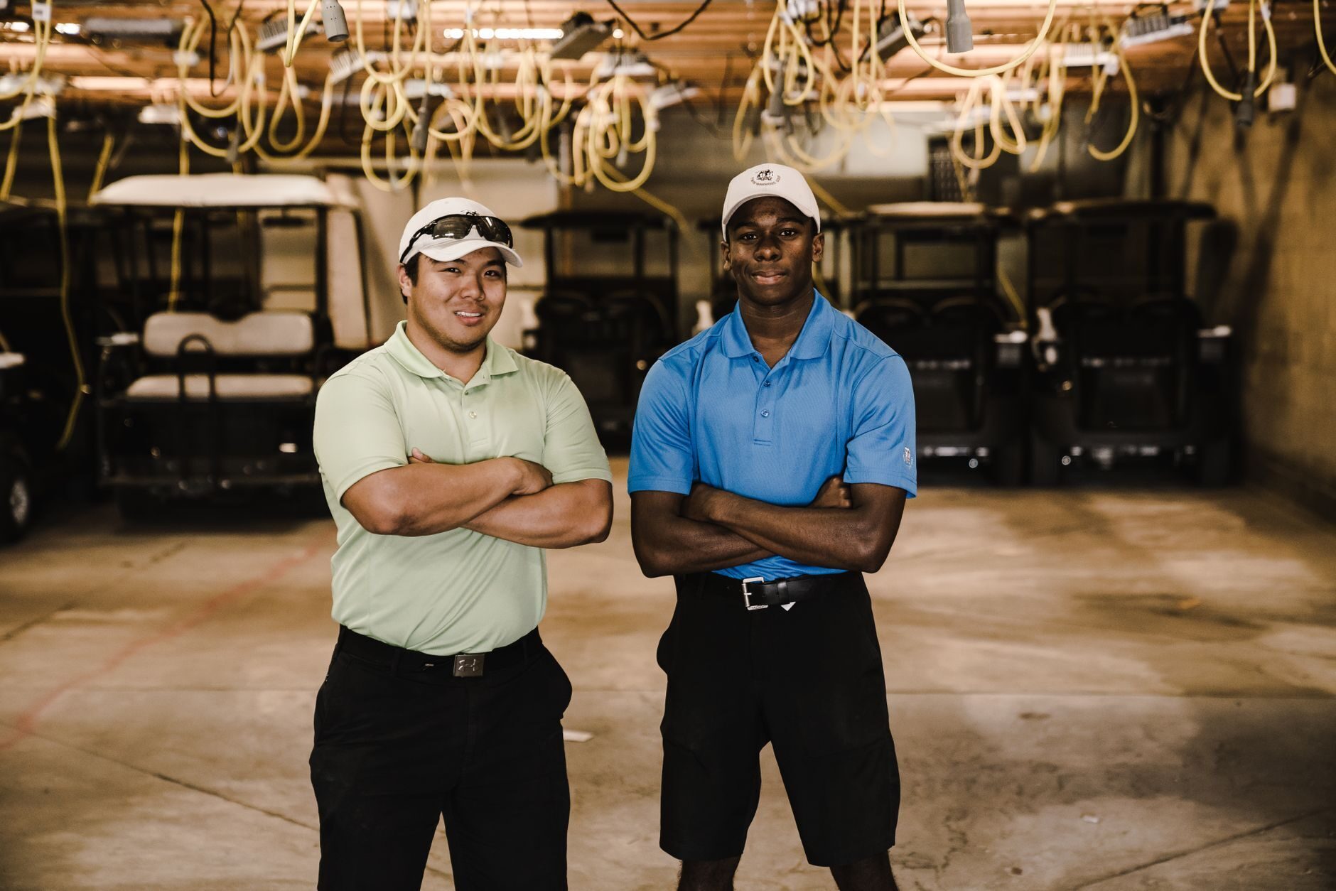 Two ICON Golf Carts service technicians standing in a warm-lit service bay with rows of carts behind them.